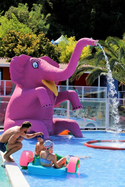 Statua di elefante rosa spruzza acqua in una piscina.