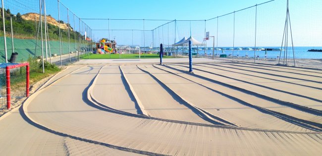 Campo da beach volley su sabbia con rete, circondato dal mare e lettini.