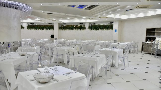 Sala da pranzo moderna con tavoli bianchi e sedie trasparenti.