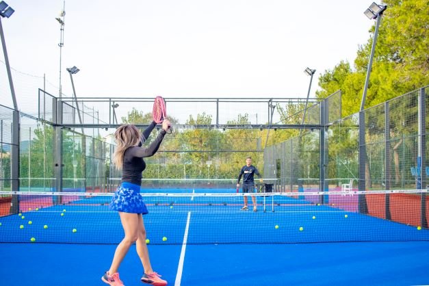 Una donna gioca a padel su un campo blu, circondata da palline, con una rete al centro.